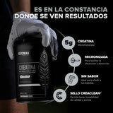 Bote de creatina monohidratada micronizada sin sabor, sostenido por una mano con guante deportivo.