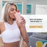 Mujer deportista tomando batido de proteínas de fresa en casa, ideal para smoothies.